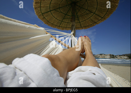 Womans' legs ona  hammock under thatched a sun shade, Mallorca, Balearic Islands, Spain Stock Photo