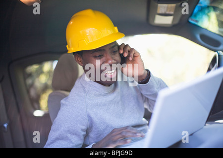 Black man wearing hard hat in vehicle using laptop Stock Photo