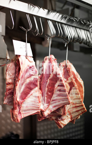 3 Chunks of beef ribs on meat hooks hanging in stainless steel kitchen or freezer Stock Photo