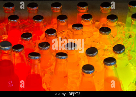A  colorful, colourful,  collection of glass soda pop bottles,soft drinks, in ice and lit from below shine with bright colors. Stock Photo