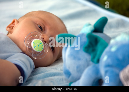 Baby boy looking at his toy with comforter in his mouth. Stock Photo