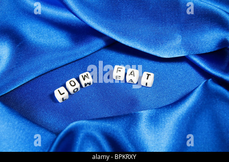 Royal blue satin background with rich folds and wrinkles for texture is the word low fat in black and white cube lettering serie Stock Photo