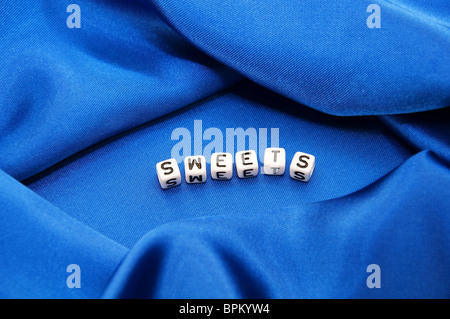Royal blue satin background with rich folds and wrinkles for texture is the word sweets in lettering in this series. Stock Photo