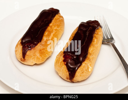 Two chocolate covered eclairs on a white plate with a fork Stock Photo