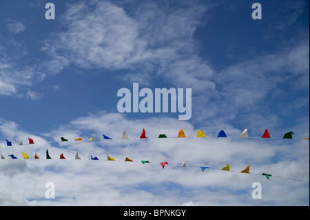 Multi colored bunting blows in the summer breeze, set against a bright blue sky complete with wispy white clouds. Stock Photo