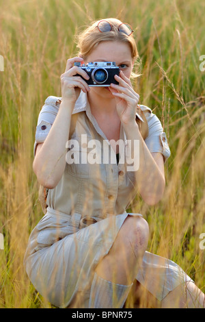 Young woman kneeling in field while taking a photograph Stock Photo