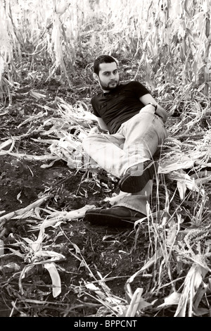 Vintage portrait of an attractive young man sitting on the ground in a corn field. Stock Photo