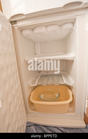 A freezer being defrosted using a bowl of hot water to melt the ice inside in the uk Stock Photo
