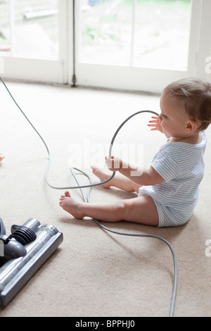 Baby on floor playing with hoover cable Stock Photo