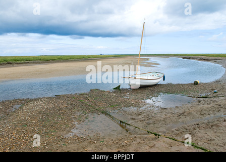 Small sailing boat on the mud flats at low tide near Blakeney point in North Norfolk. Stock Photo