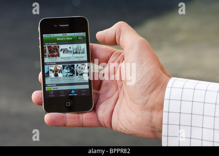 The iPhone 4 in the palm of the hand of a man. On the screen you can see the Spotify app. Stock Photo