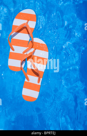 Pretty pair of stripey flip flops or thongs in a sparkling blue swimming pool Stock Photo