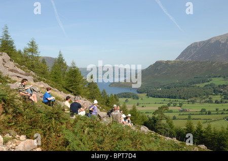 Group of walkers resting at Old Burtness on their way up Red Pike on a sunny day under  a blue sky with Crummock Water behind. Stock Photo