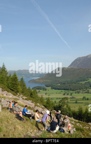 Group of walkers resting at Old Burtness on their way up Red Pike on a sunny day under  a blue sky with Crummock Water behind. Stock Photo