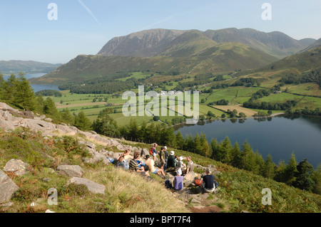 Group of walkers resting at Old Burtness on their way up Red Pike on a sunny day under  a blue sky with Crummock Water behind. Stock Photo