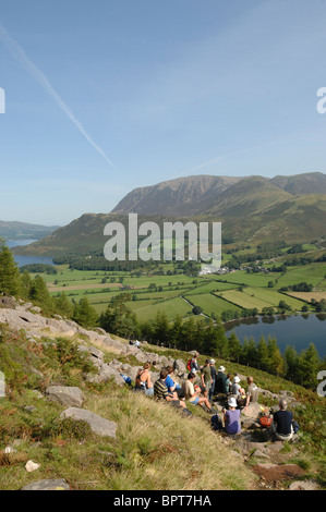 Group of walkers resting at Old Burtness on their way up Red Pike on a sunny day under  a blue sky with Crummock Water behind. Stock Photo