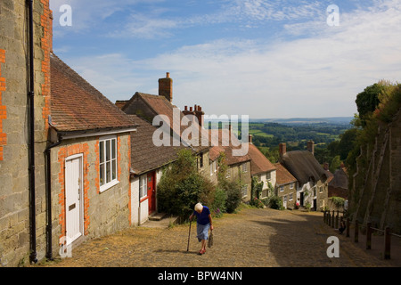 An old woman walks with the aid os a stick to the top of Gold Hill in Dorset made famous by an Hovis bread Television Adveriseme Stock Photo