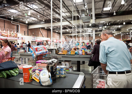 people pass through rows of checkout counters loaded with consumer purchases at a Costco USA  big box retailer Stock Photo