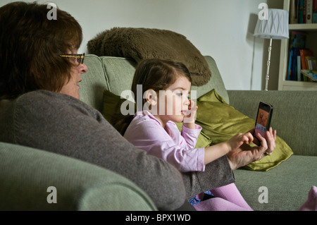 dh Granny and grandchild GIRL UK playing with Iphone computer game grandmother child young children kids Stock Photo