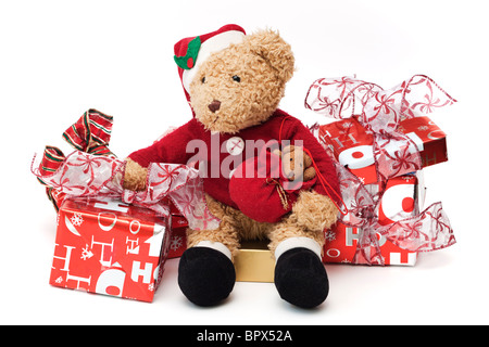 Teddy at Christmas. Well loved child's teddy dressed as Santa Claus sitting among wrapped Christmas presents. Stock Photo