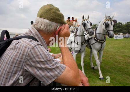 A man wearing a hearing aid watches a horse and carriage display. Stock Photo