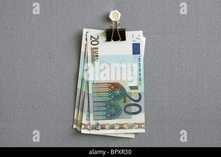20 euro notes hanging from a bulldog clip against a blue cloth background Stock Photo