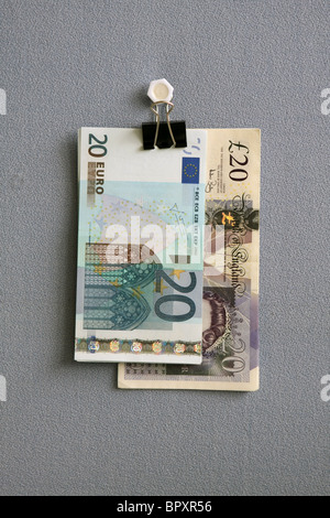 £20 and 20 euro notes hanging from a bulldog clip against a blue cloth background Stock Photo
