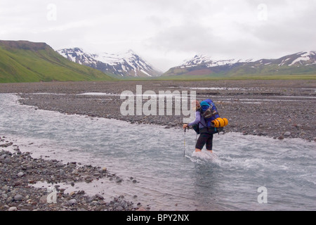 A woman crossing a river on Umnak Island in the Aleutian Islands. Stock Photo