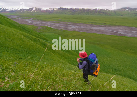 A woman hiking up a ridge above a river on Umnak Island in the Aleutian Islands. Stock Photo