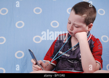 Bored boy of eight plays a game on his mobilr phone now a full entertainment centre. Model Release Available Stock Photo