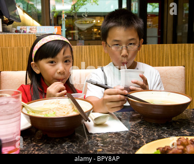 Chinese brother and sister drinking soda and eating wonton noodle soup at restaurant Stock Photo