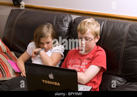 An 8 year old girl and 11 year old boy concentrate on a laptop computer Stock Photo