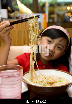 Young Chinese girl playing with food and eating wonton noodle soup at restaurant Stock Photo