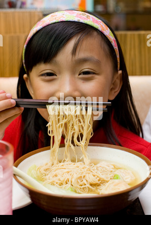 Young Chinese girl playing with food and eating wonton soup at restaurant Stock Photo