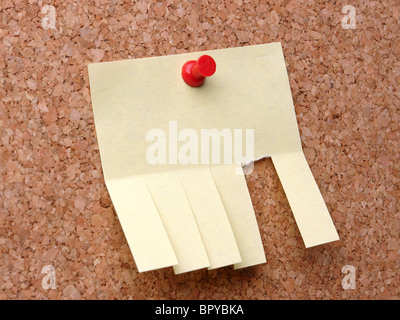 Blank yellow post-it note with cut slips affixed to corkboard with red pushpin Stock Photo