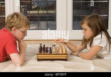 An eleven year old boy and eight year old girl play chess at home Stock Photo
