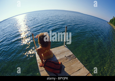 Woman sitting on dock by lakeside. Summer. Ontario, Canada. Stock Photo