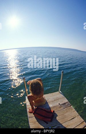 Woman sitting on dock by lakeside. Summer. Ontario, Canada. Stock Photo