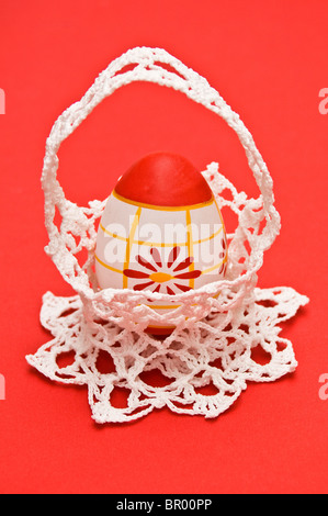 Easter egg in white crochet basket isolated on red, portrait Stock Photo