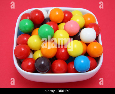 Colorful gumball candy in white bowl on red surface Stock Photo