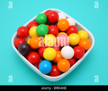 Colourful gumballs in white bowl on blue surface Stock Photo