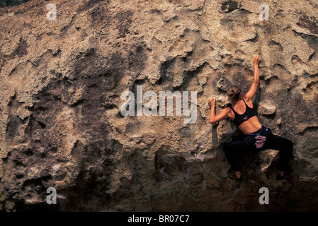 A female rock climber boulders on a bouldering route in a remote climbing area. Stock Photo