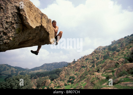 A male rock climber attempts to get over the top of an overhanging bouldering route in a remote climbing area. Stock Photo