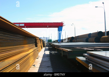 Big diameter ferrous metal pipes and steel sheets loading on the storage yard. Stock Photo