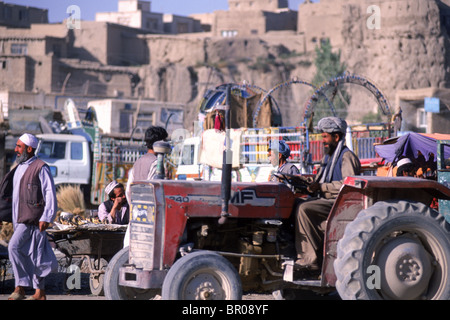 A tractor drives through a bustling market that flourishes below the old city walls in the town of Ghazni, Afghanistan. Stock Photo