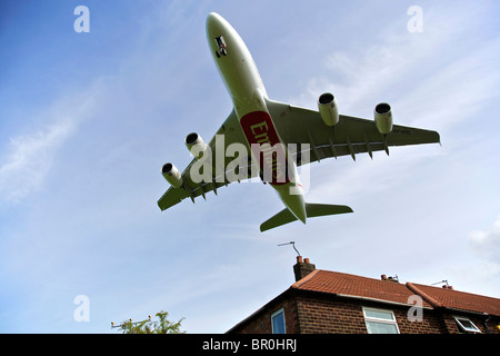 Emirates airline Airbus A380 arrives at Manchester airport, flying low over house rooftop. Stock Photo