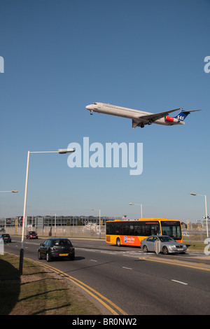 A SAS plane coming in to land at Heathrow Airport, London, passing over buses and cars on the perimeter road. Stock Photo