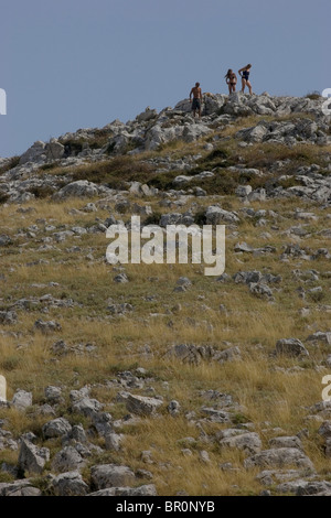 Three people climb a grass and rock-covered hill on an islands in Kornati National Park in the Adriatic. Stock Photo