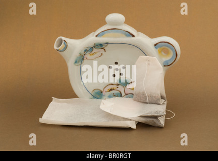 Teapot teabag holder with drain holes standing up on counter with a display of teabags in various shapes and sizes. Stock Photo