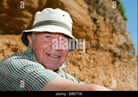 Elderly man wearing a hat sitting outdoors on a summers day smiling. Stock Photo